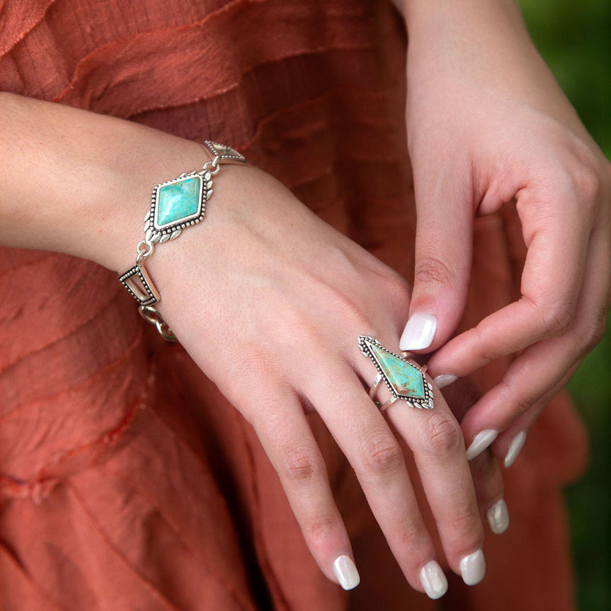 Close-up of hands wearing turquoise gemstone jewelry against a rust-colored fabric background