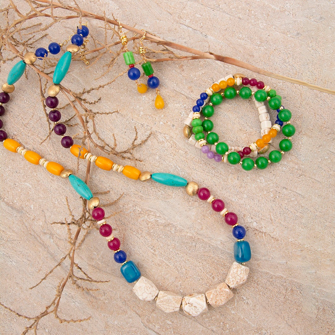 Colorful beaded necklace and bracelet on a textured surface with branches.