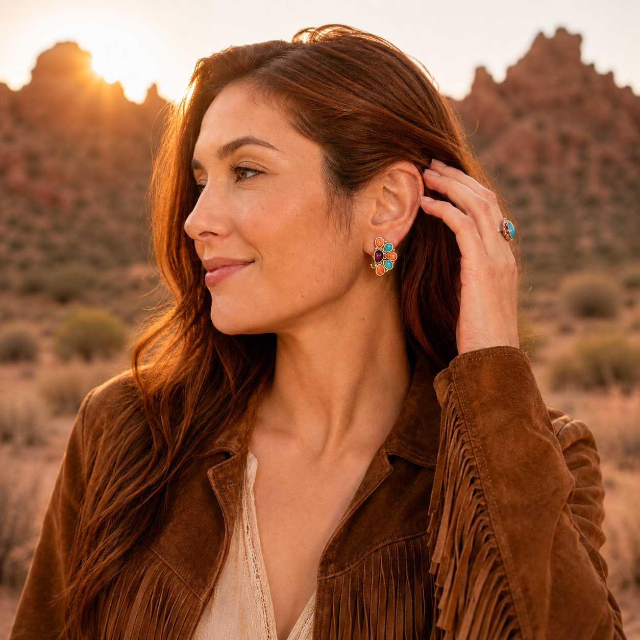 Woman in a brown suede jacket with colorful earrings against a desert sunset.