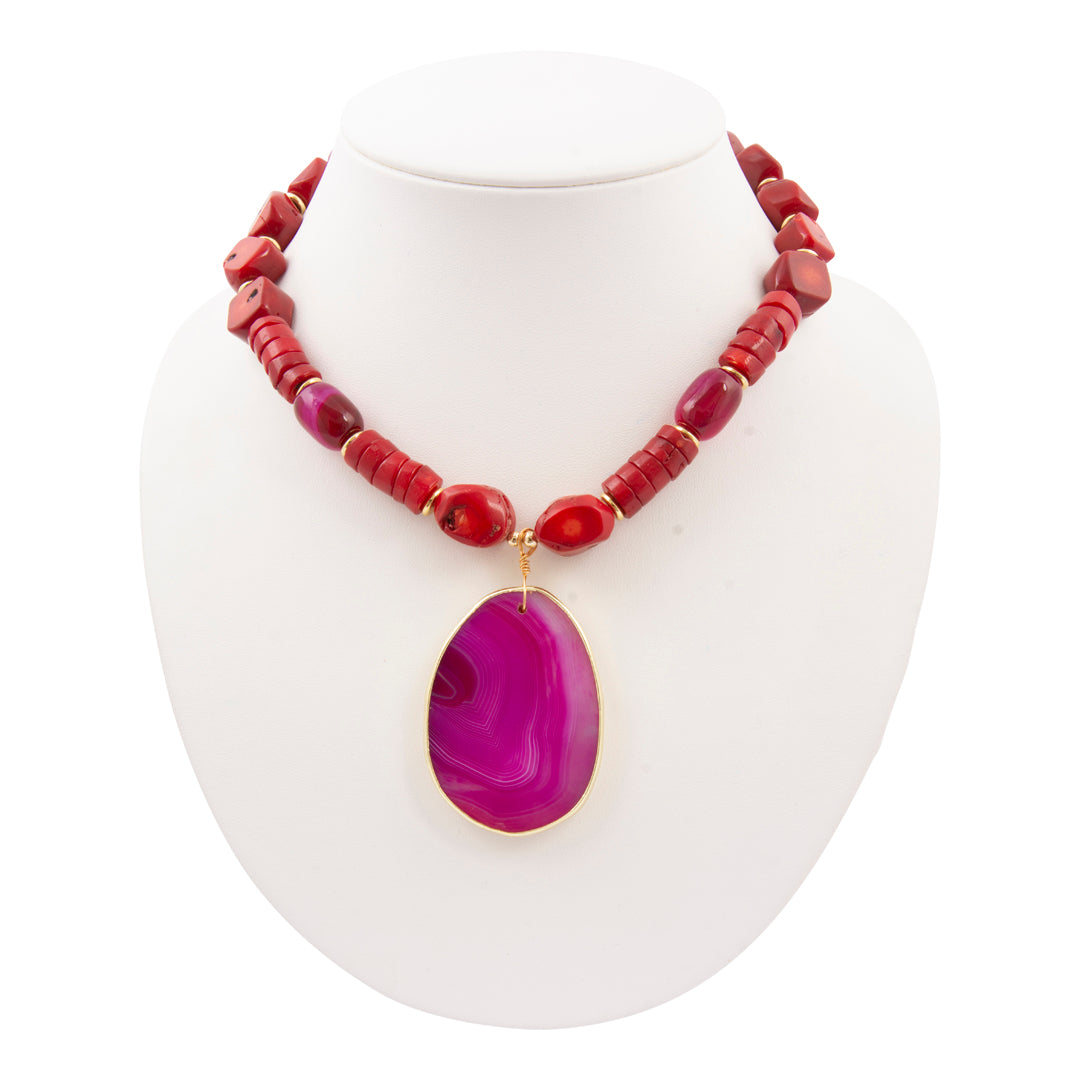 Necklace with red beads and a purple pendant on a white stand