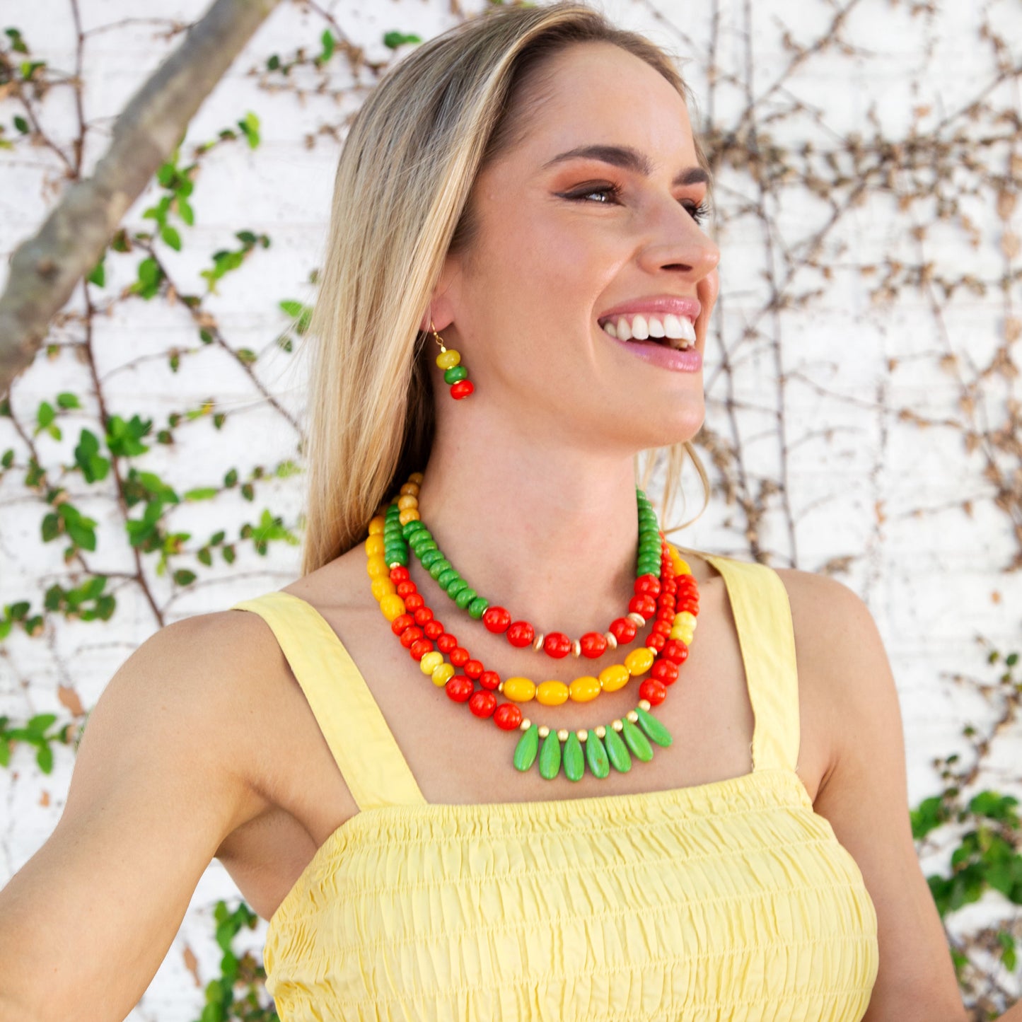 Woman wearing a colorful necklace and yellow top against a natural background