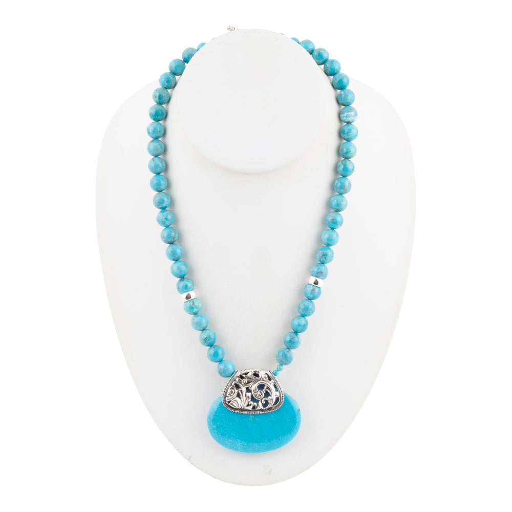 A turquoise beaded necklace with a silver-toned cloud-shaped pendant featuring clear rhinestones, displayed on a white jewelry bust.