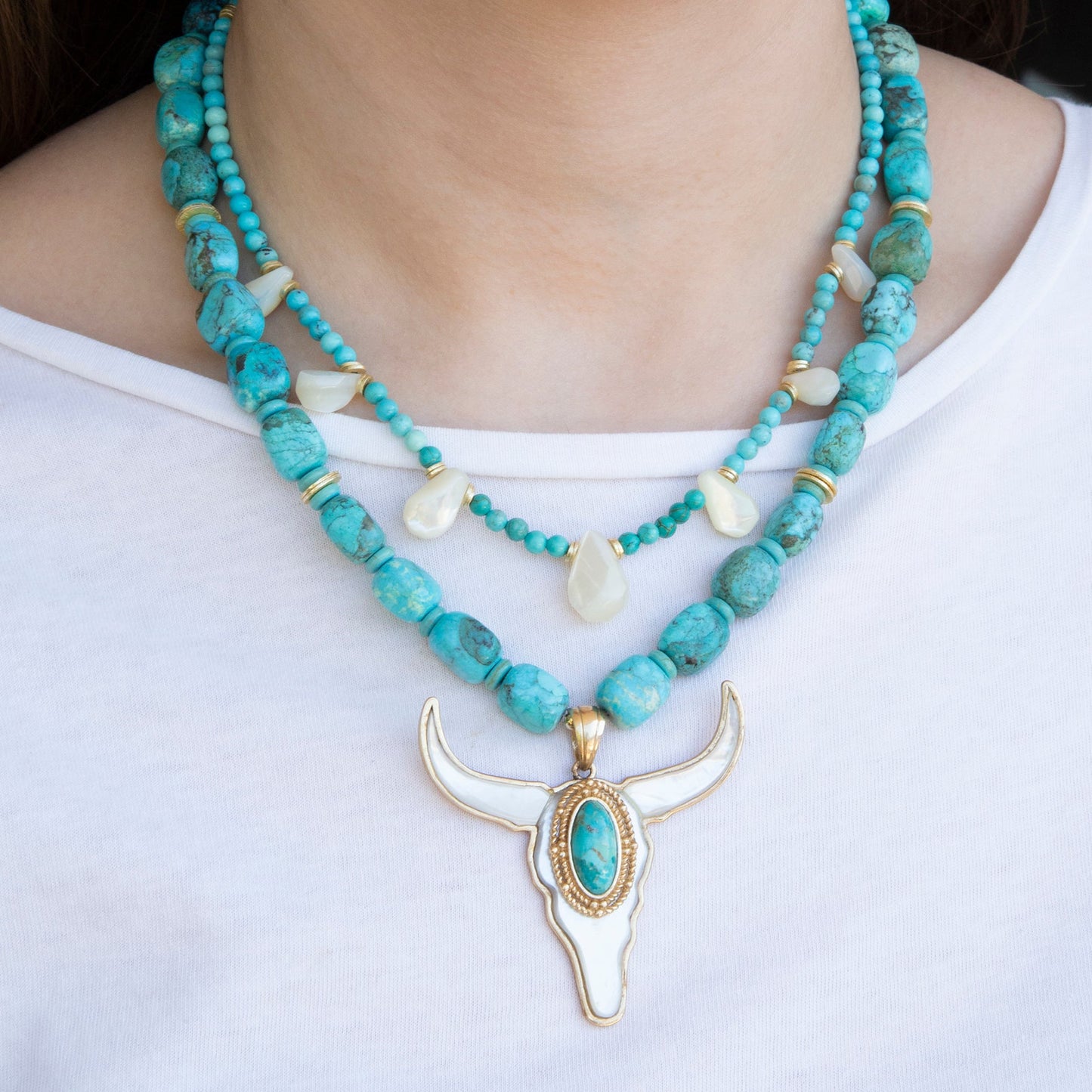 Turquoise beaded necklace with a gold bull head pendant on a white background