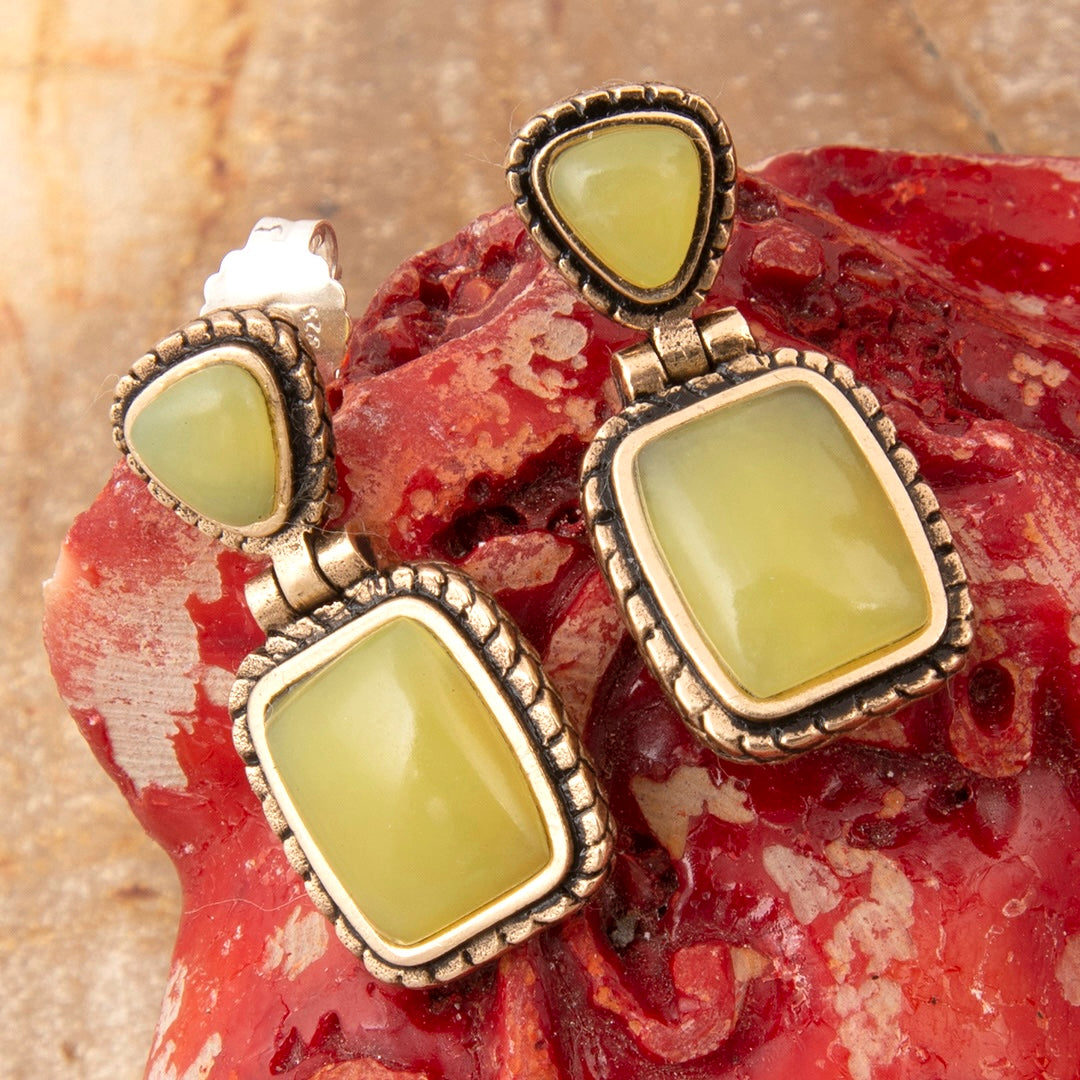 Pair of earrings with green stones and gold accents on a textured red and beige background