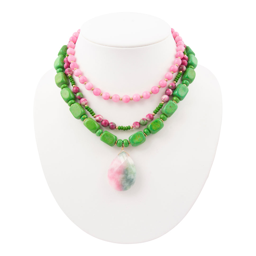 Two necklaces with pink and green beads on a white stand.