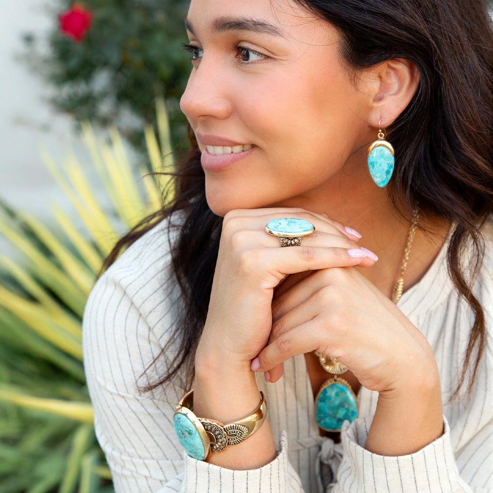 Woman wearing turquoise jewelry with a blurred green plant background
