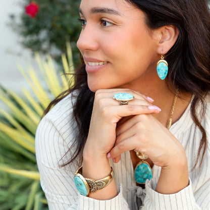 Woman wearing turquoise jewelry with a blurred green plant background