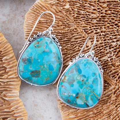 Turquoise earrings with silver hooks on a textured beige surface