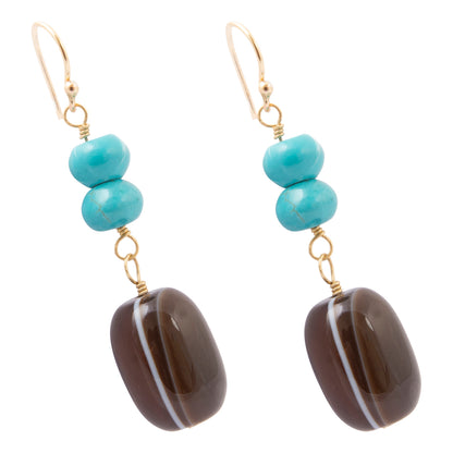 A pair of gold-tone dangle earrings featuring three stacked turquoise beads and a large, polished dark brown agate drop with a white band, set against a plain white background.