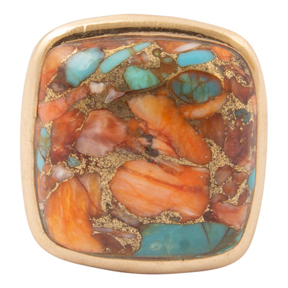 A square gold-toned ring featuring a colorful inlay of orange, turquoise blue, brown, and gold flecks, set against a plain white background.