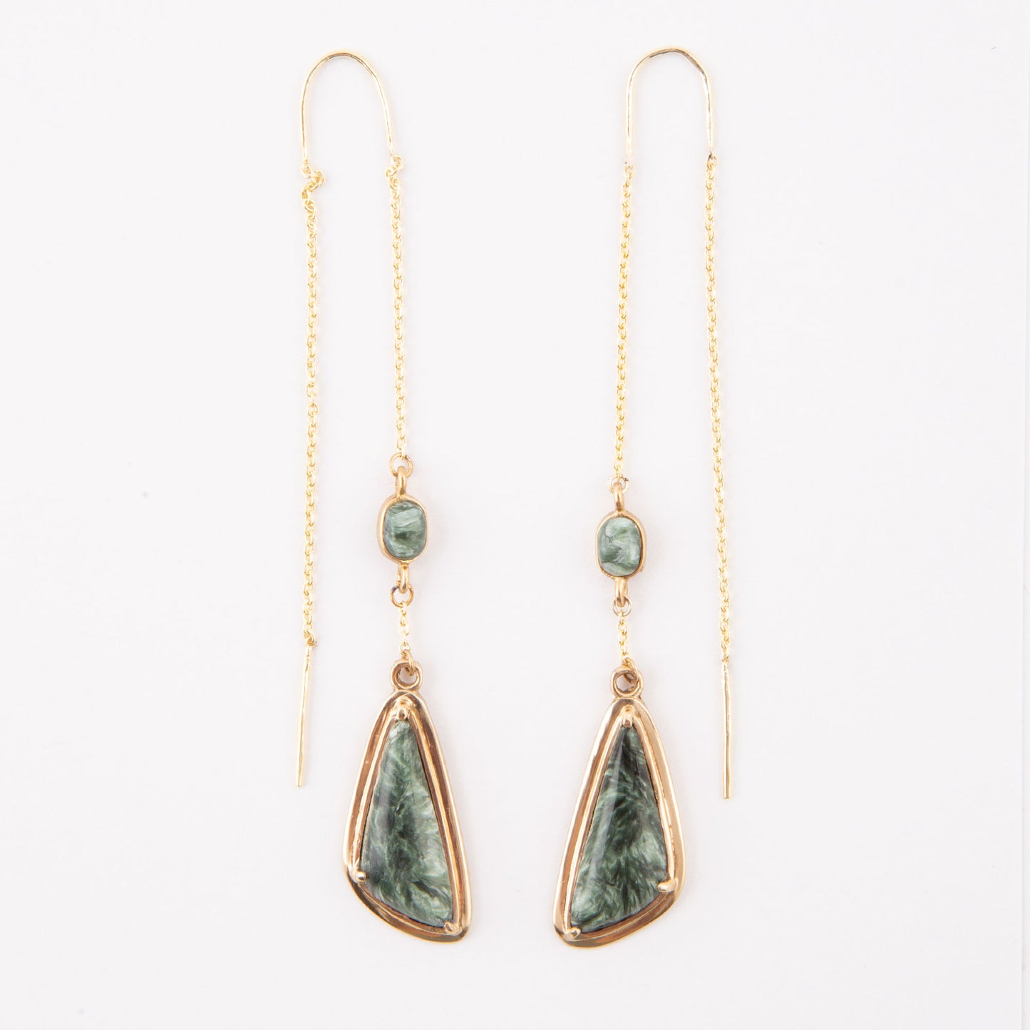A pair of gold drop earrings featuring a small round green stone and a larger teardrop-shaped green stone with a gold border, hanging from delicate gold chains on a white background.