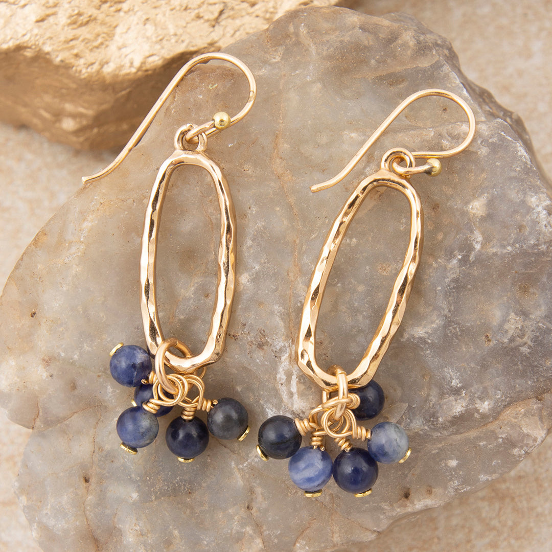 Gold hoop earrings with blue beads on a stone background