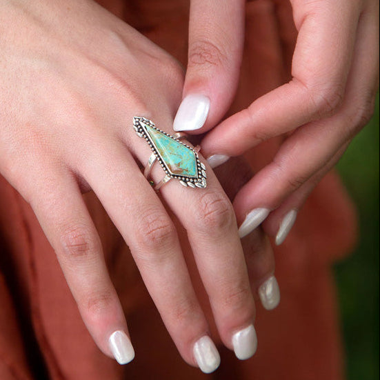 Close-up of hands wearing turquoise gemstone jewelry against a rust-colored fabric background