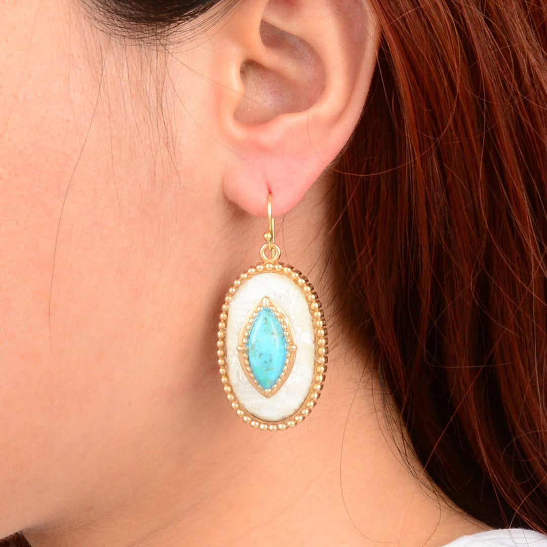 Close-up of an ear wearing a gold and turquoise earring with red hair in the background