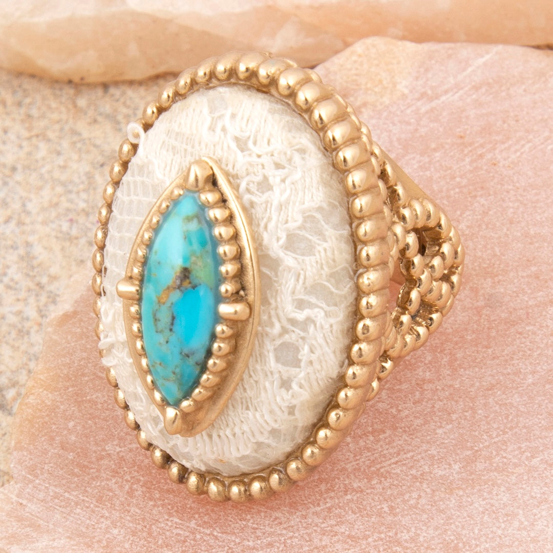Gold ring with a turquoise stone on a textured beige surface