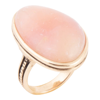 A gold ring featuring a large, smooth, oval-shaped pale pink stone, set against a plain white background.