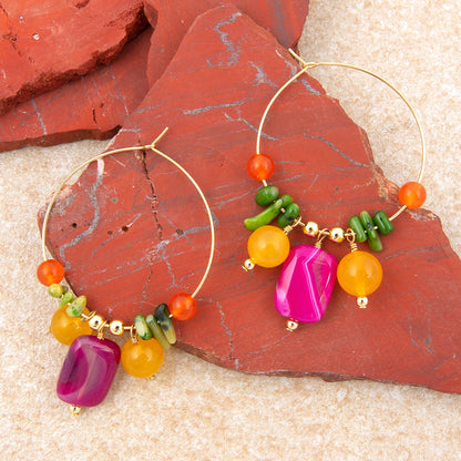 Gold hoop earrings with colorful beads on a textured surface