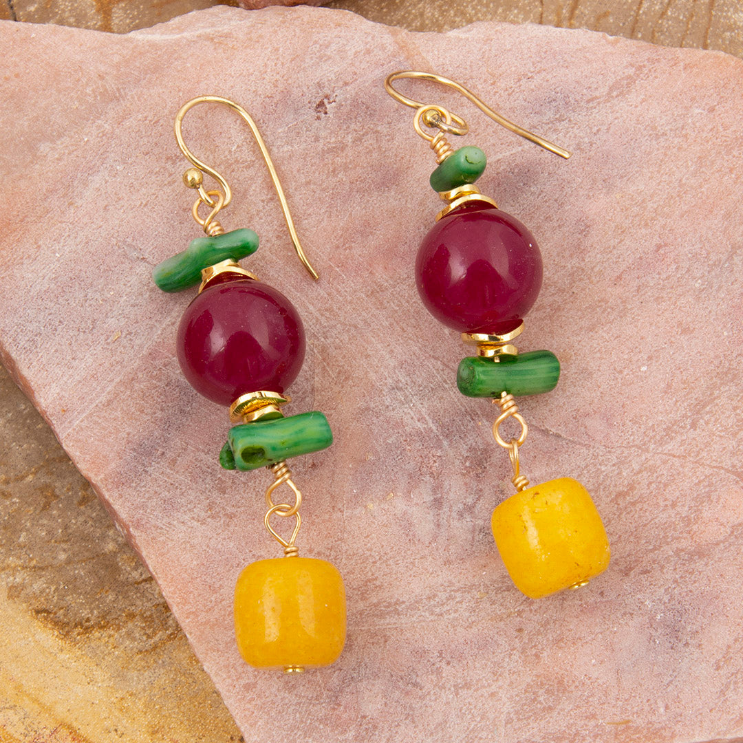 Pair of earrings with red, green, and yellow beads on a stone surface