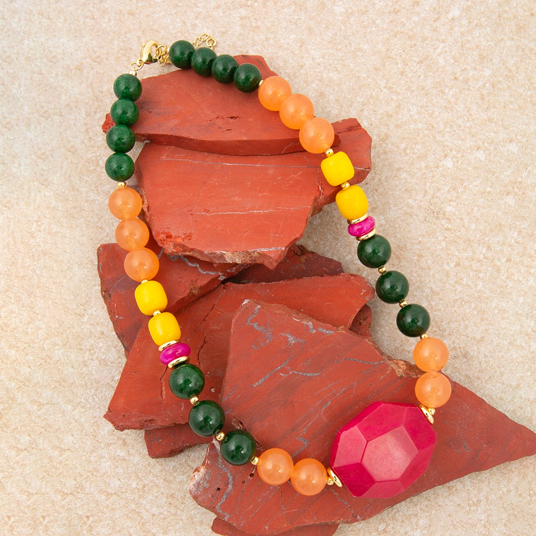 Colorful beaded bracelet with a large pink gemstone on a textured surface