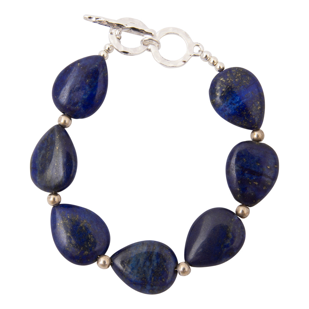 A beaded bracelet featuring seven polished dark blue lapis lazuli stones and small metallic spacer beads, connected by a silver-toned toggle clasp on a plain white background.