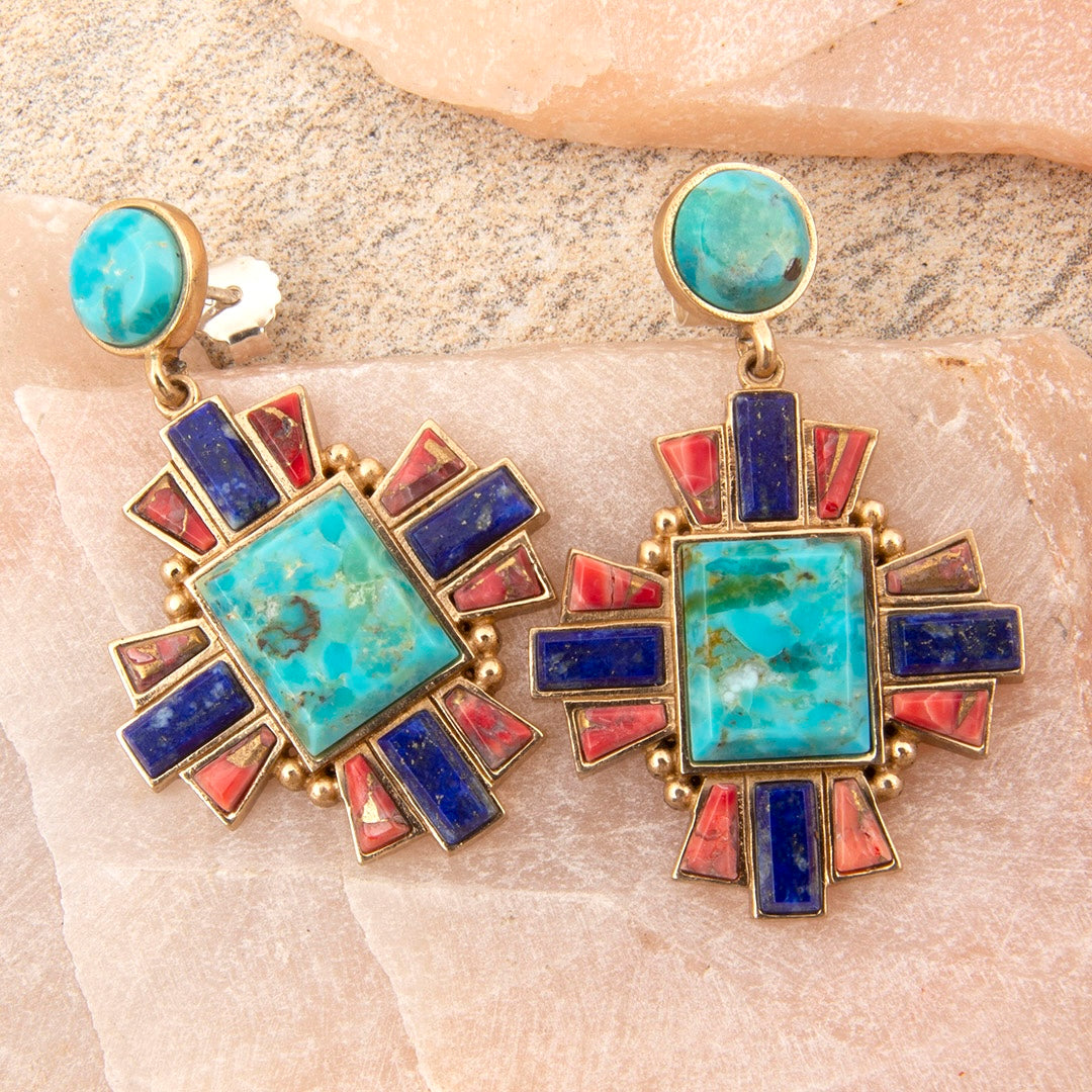 Colorful earrings with turquoise, red, and blue stones on a stone surface