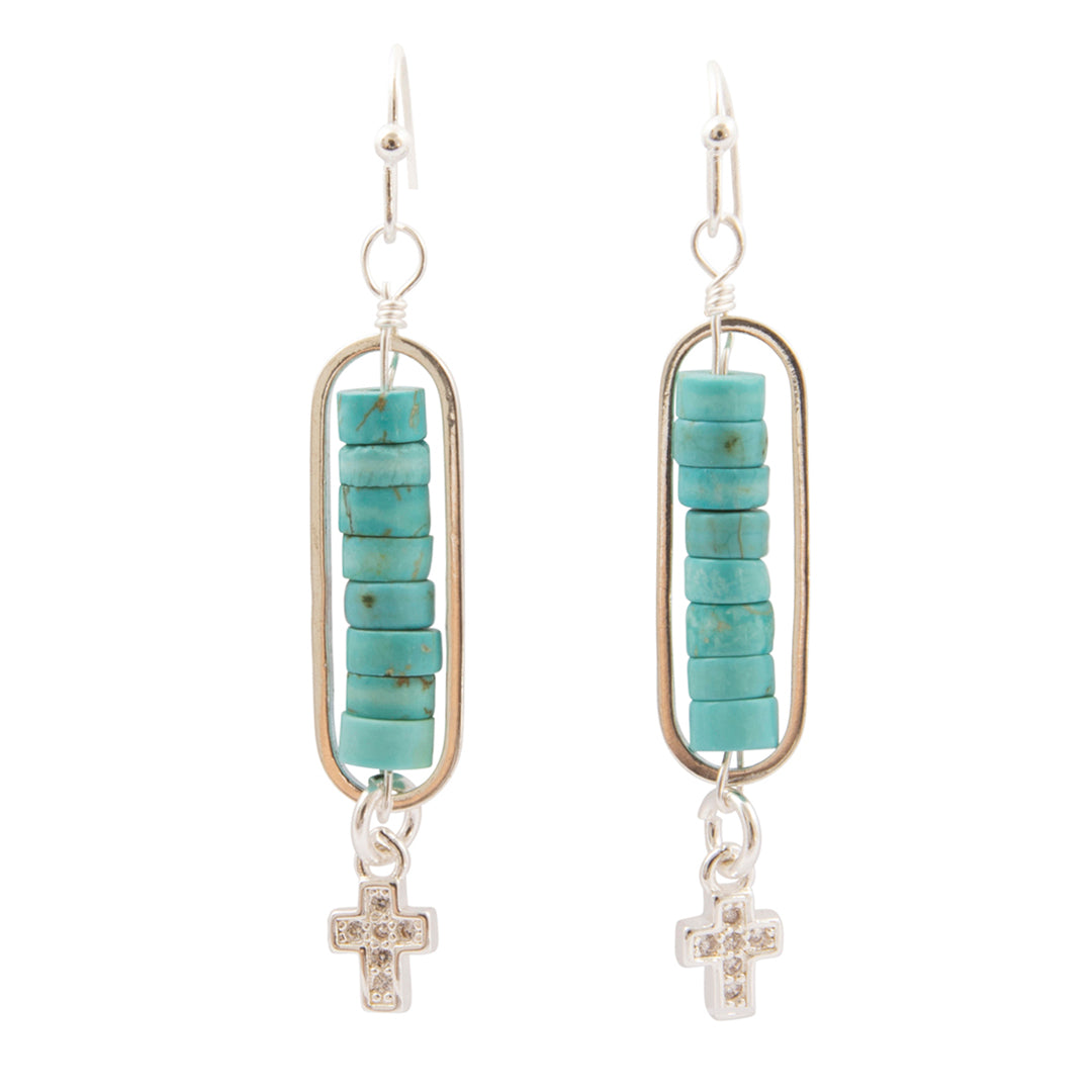 A pair of silver dangle earrings featuring a vertical bar with a stack of turquoise beads and a small silver cross charm adorned with clear rhinestones, shown against a plain white background.