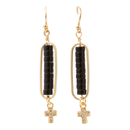 A pair of gold drop earrings featuring a vertical bar of black beads, a small gold wire frame, and a dangling cross charm embellished with clear crystals, set against a plain white background.