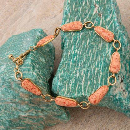 Bracelet with pink stone beads on gold chain against a textured green stone background
