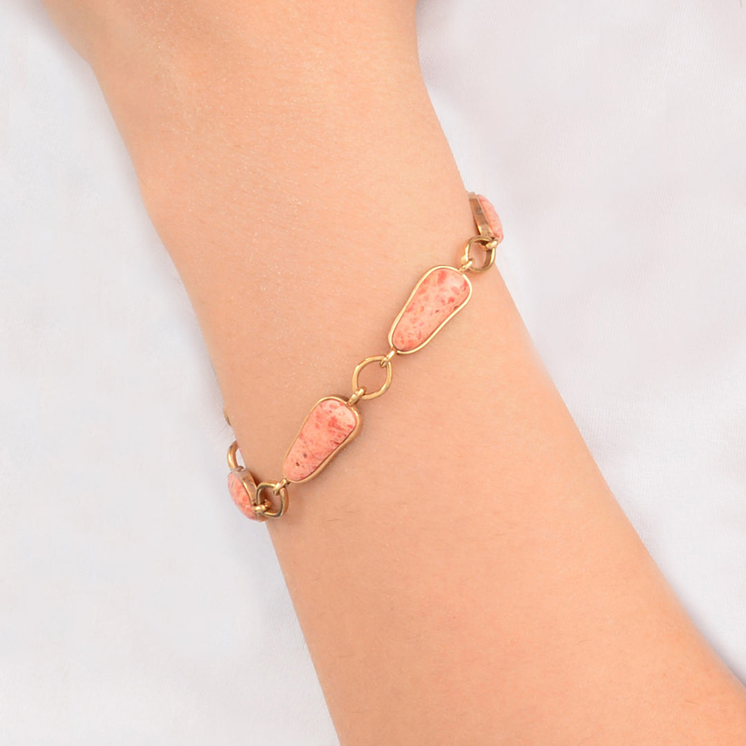 Gold bracelet with pink stones on a wrist against a white background