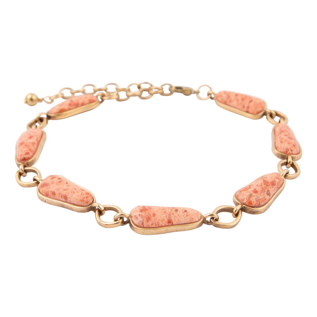 Gold bracelet with coral-colored stones on a white background
