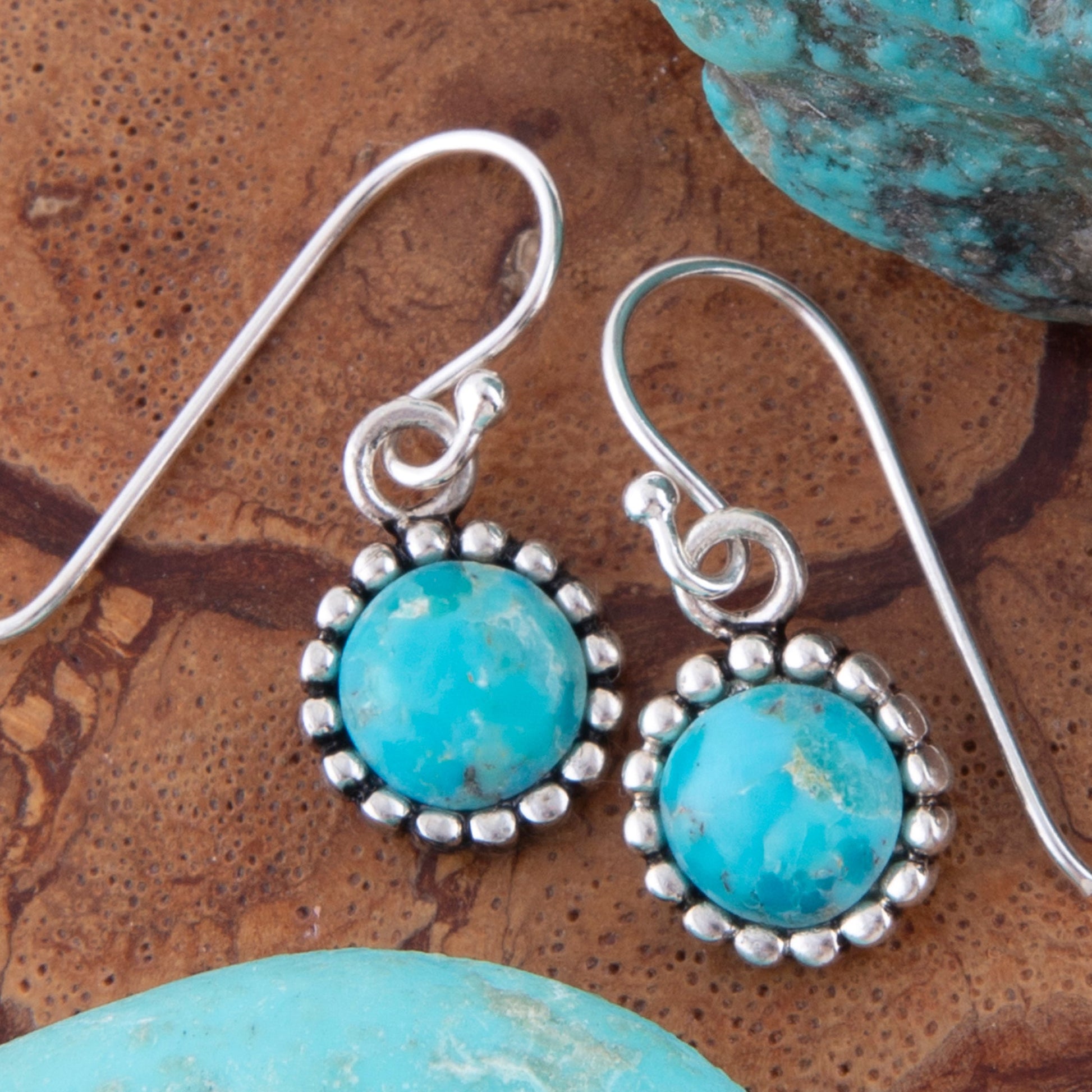 Turquoise stone earrings with silver settings on a textured brown surface.