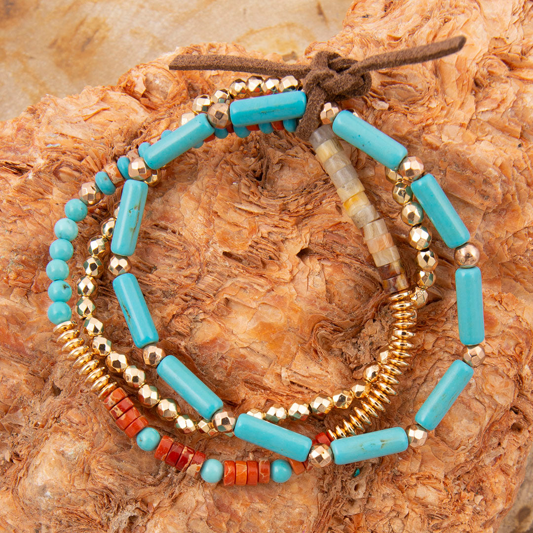 Stack of beaded bracelets with turquoise, gold, and red beads on a textured surface