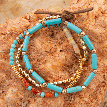 Stack of beaded bracelets with turquoise, gold, and red beads on a textured surface