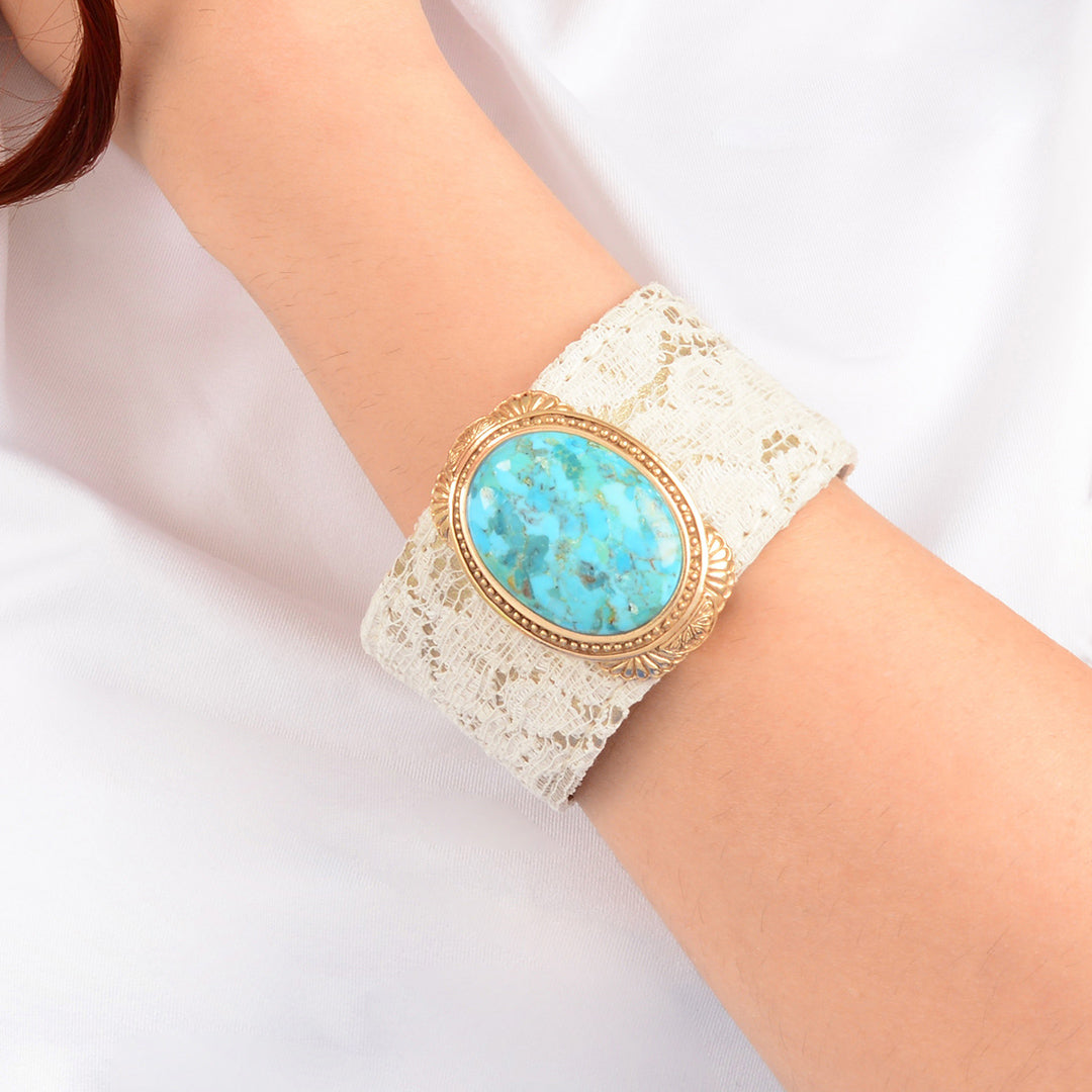 Turquoise stone bracelet on a white lace cuff worn on a wrist against a white background