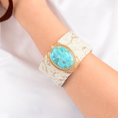 Turquoise stone bracelet on a white lace cuff worn on a wrist against a white background