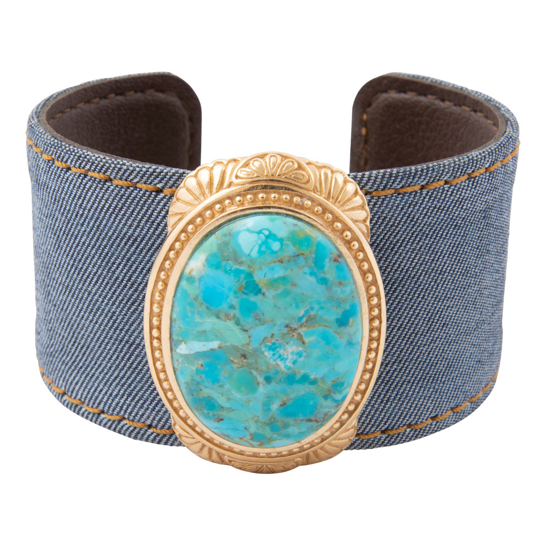 Denim cuff bracelet with a turquoise stone and gold frame on a white background
