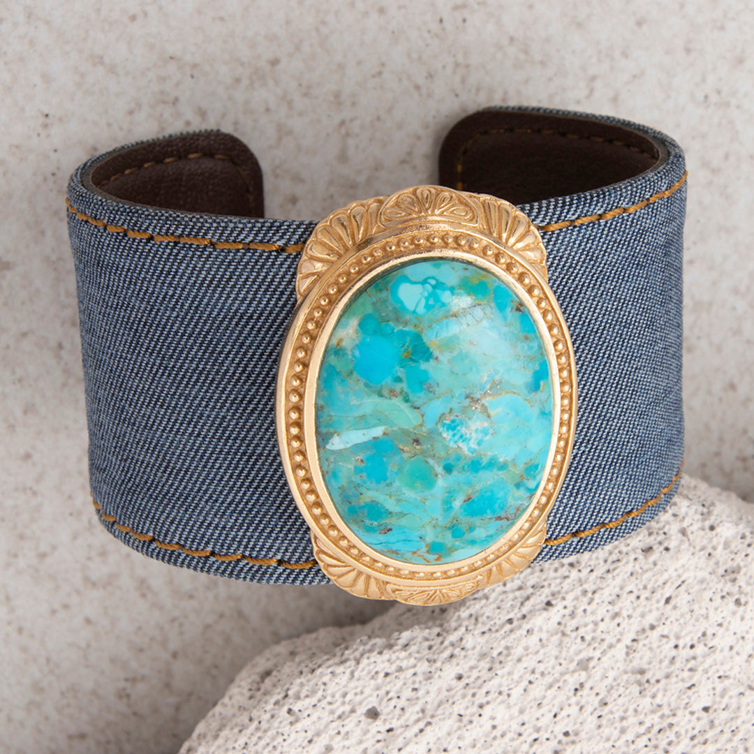 Denim cuff bracelet with turquoise stone and gold accents on a textured surface