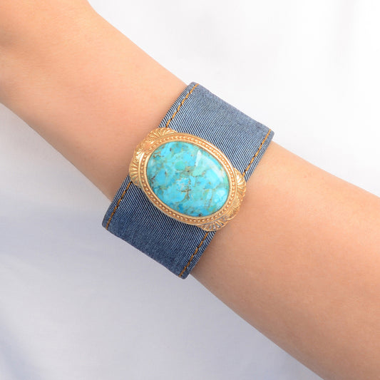 Denim bracelet with turquoise stone and gold accents on a wrist against a light background
