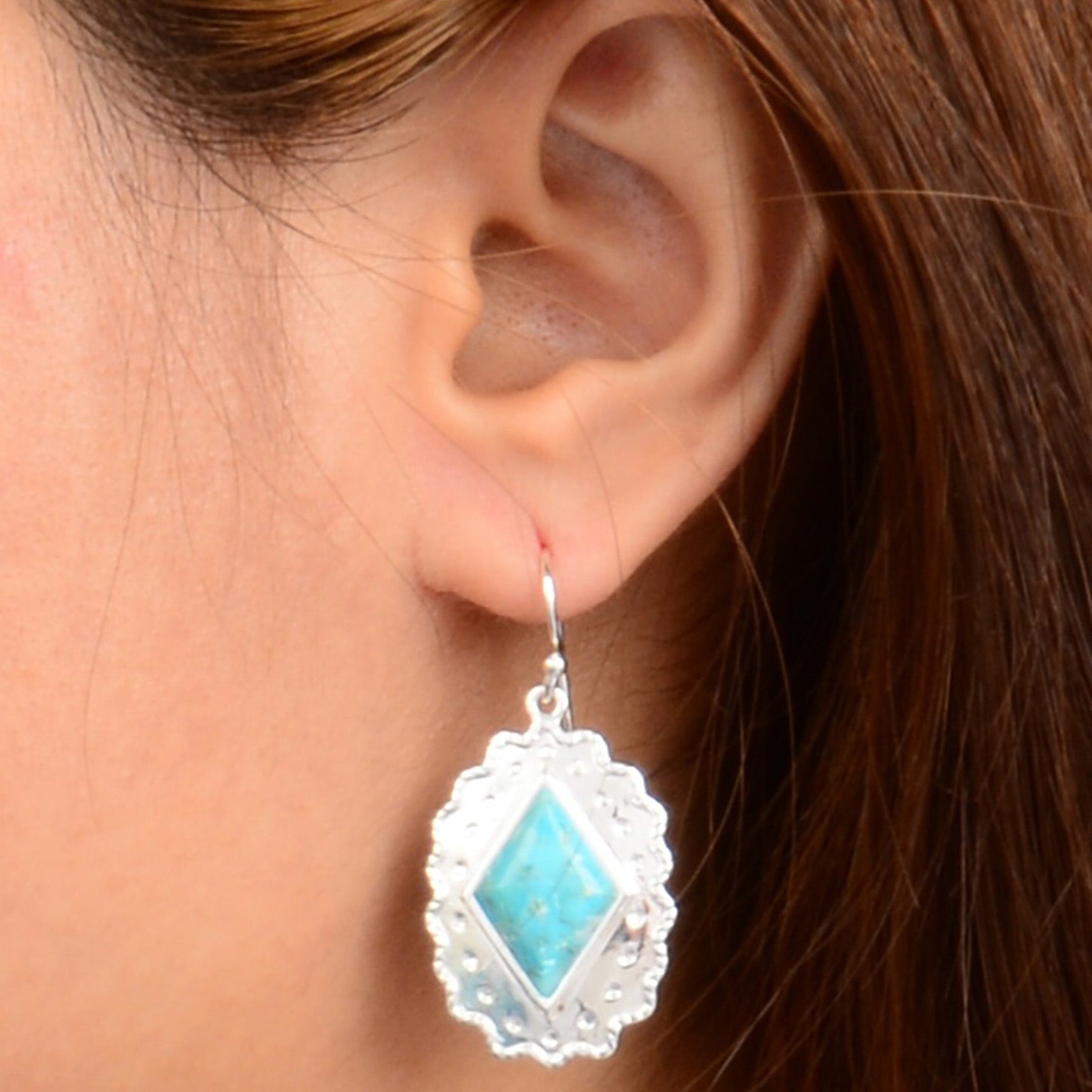 Close-up of an ear wearing a turquoise earring with a silver frame.