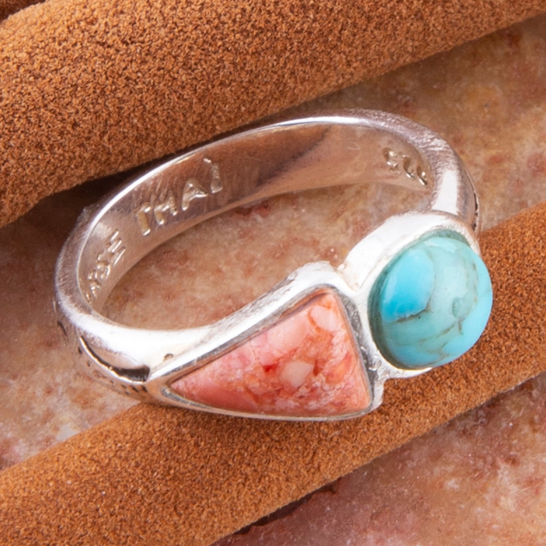 Silver ring with turquoise and pink stone on a brown surface
