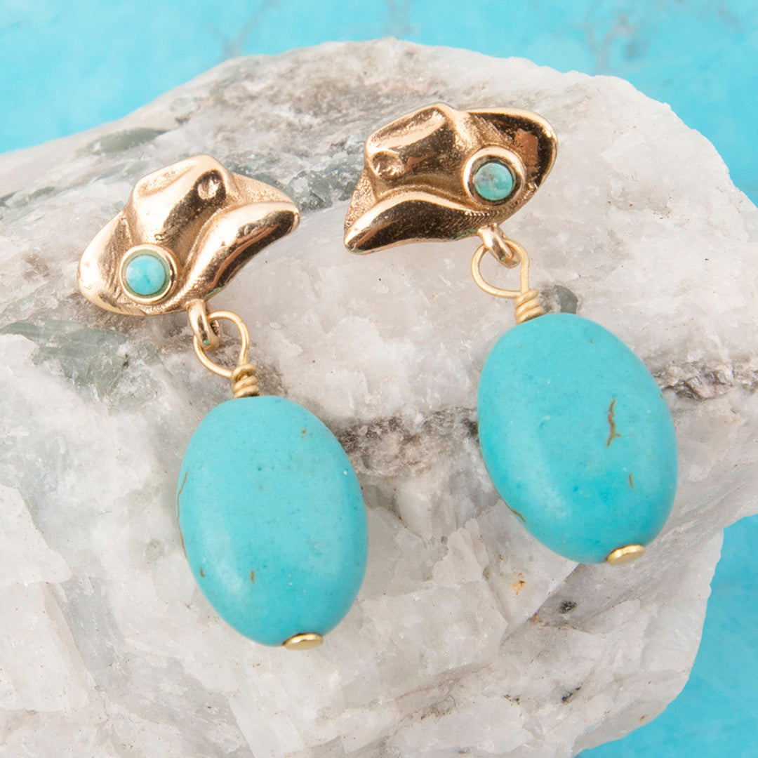 Gold earrings with turquoise stones on a stone surface