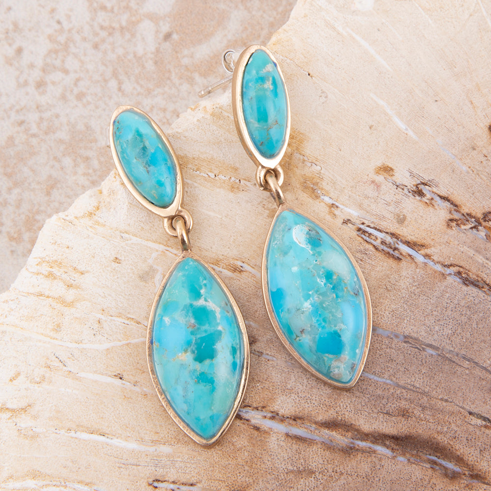 Turquoise stone earrings on a textured beige surface
