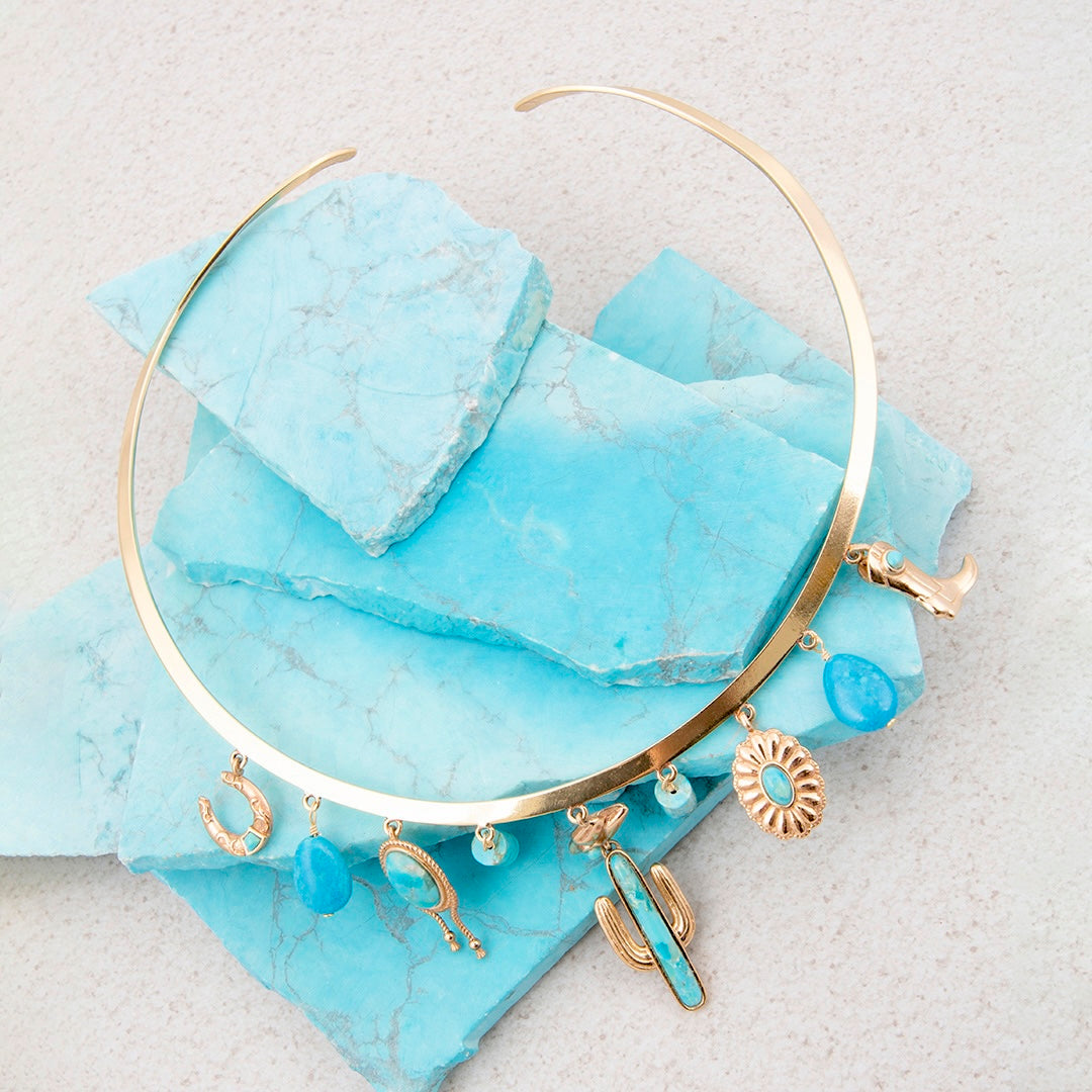 Gold choker necklace with turquoise stones on a light blue marble surface