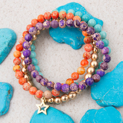 Stack of colorful beaded bracelets with a star charm on a textured surface with blue stones.