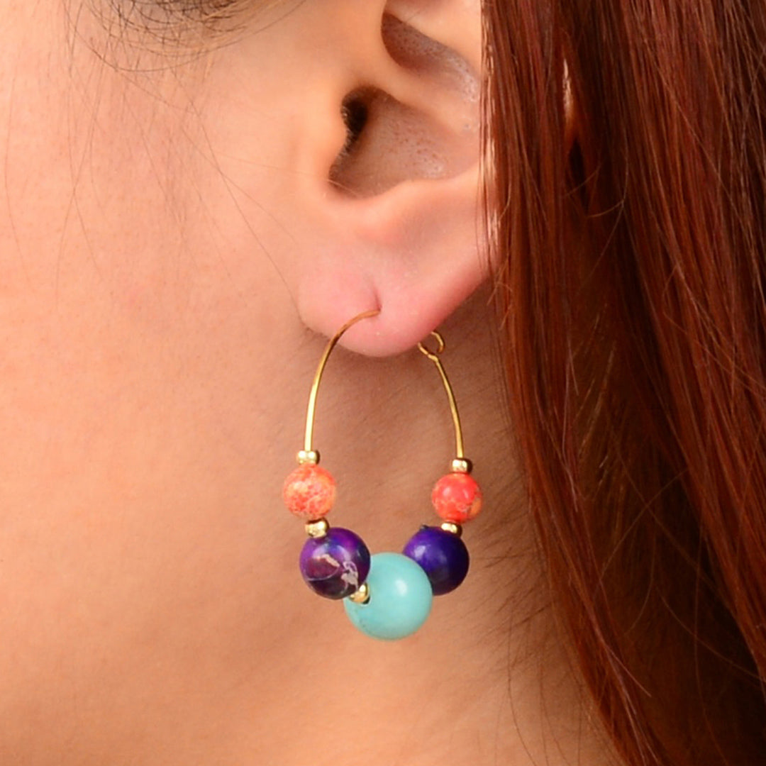 Close-up of a person wearing colorful beaded hoop earrings.