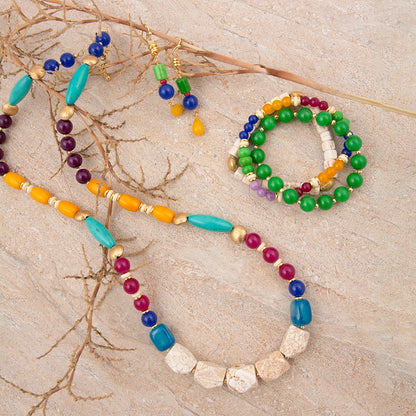 Colorful beaded necklace and bracelet on a textured surface with branches.