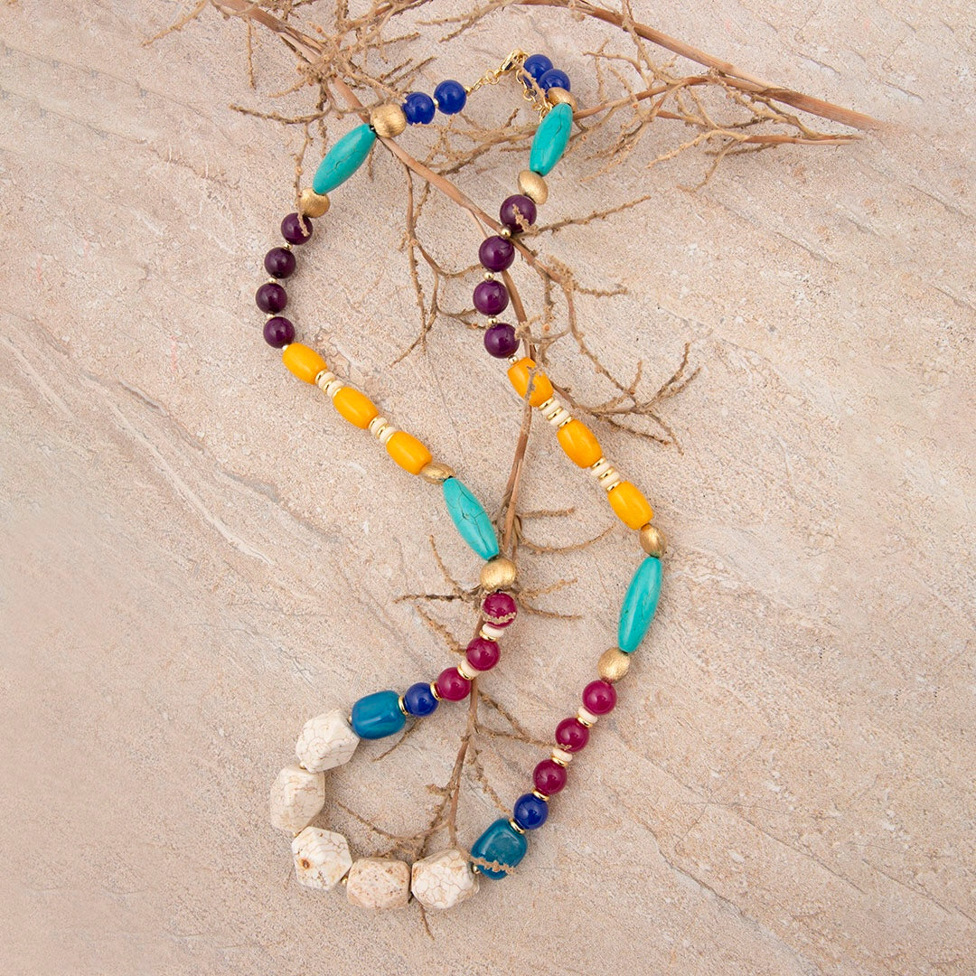 Colorful beaded necklace on a textured beige surface with branches.