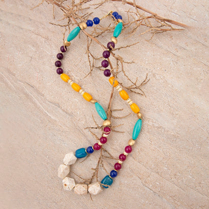 Colorful beaded necklace on a textured beige surface with branches.