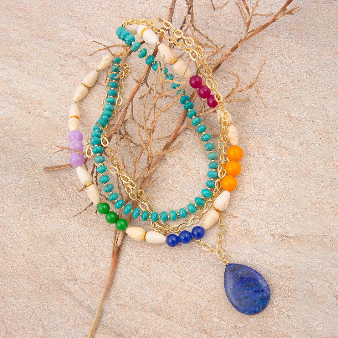 Stack of colorful beaded bracelets on a textured surface with branches.