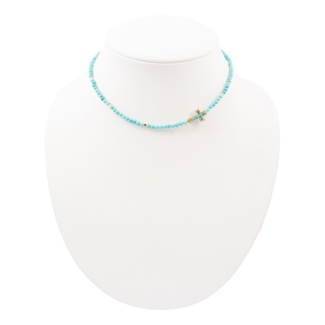 Necklace with turquoise beads and a small cross on a white mannequin.
